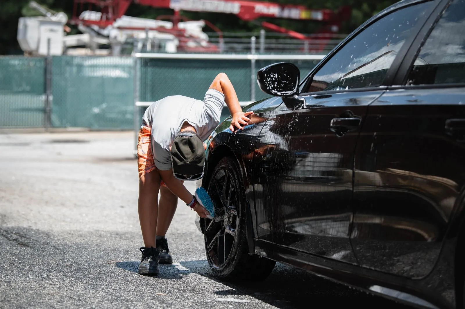 A person cleans a black car's wheels during a sunny day outdoors.